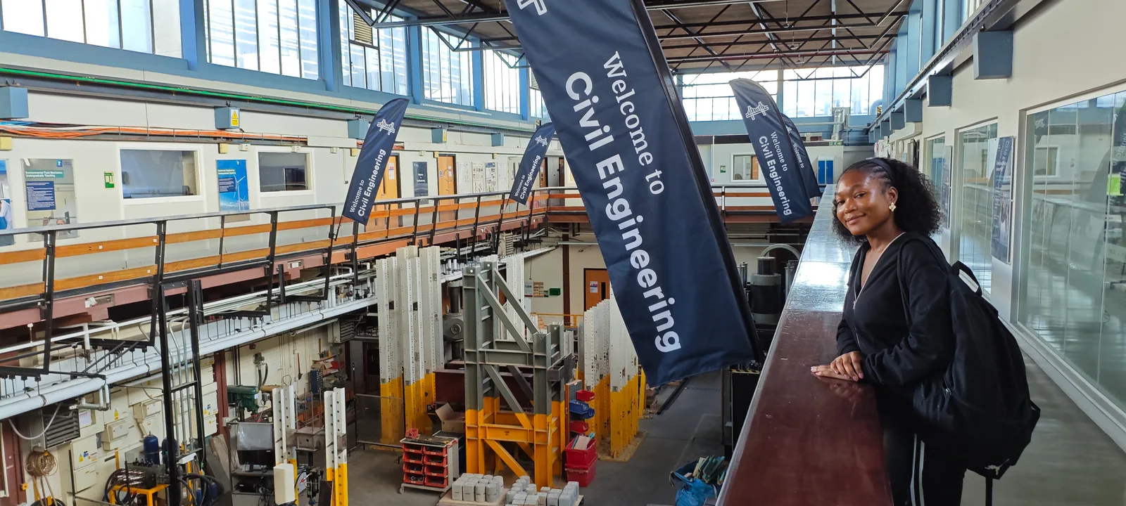 Timi Adepegba in the structures laboratory at the University of Nottingham, beside a 'Welcome to Civil Engineering' banner
